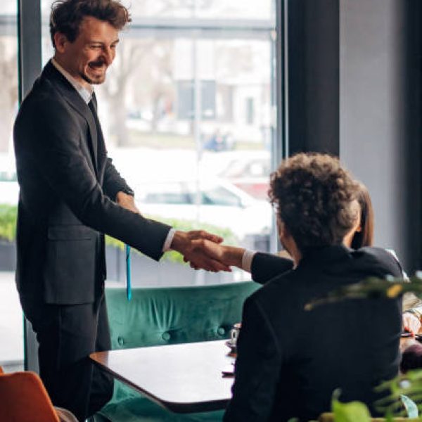 A business man joins a small group of his colleagues in a restaurant for a meeting and shakes hands with them